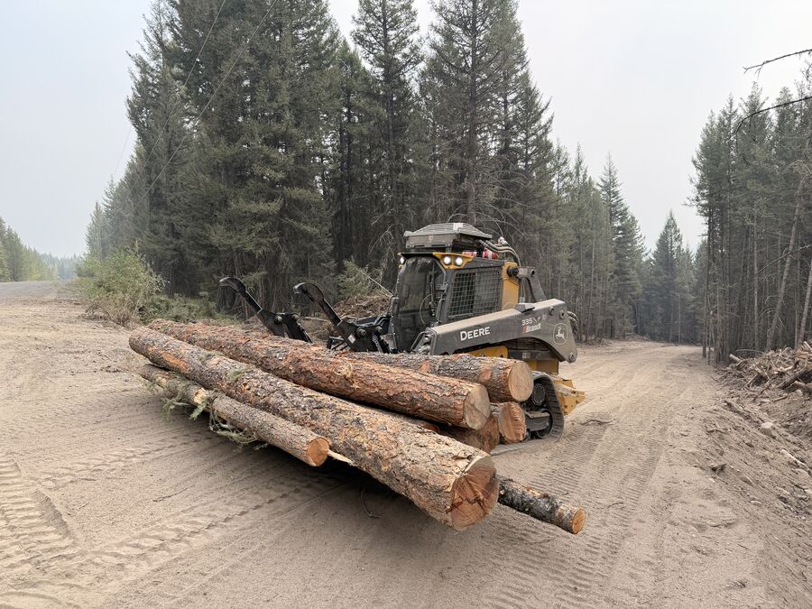 John Deere 335P track loader with forestry guarding and grapple, moving decked timber on a forest road